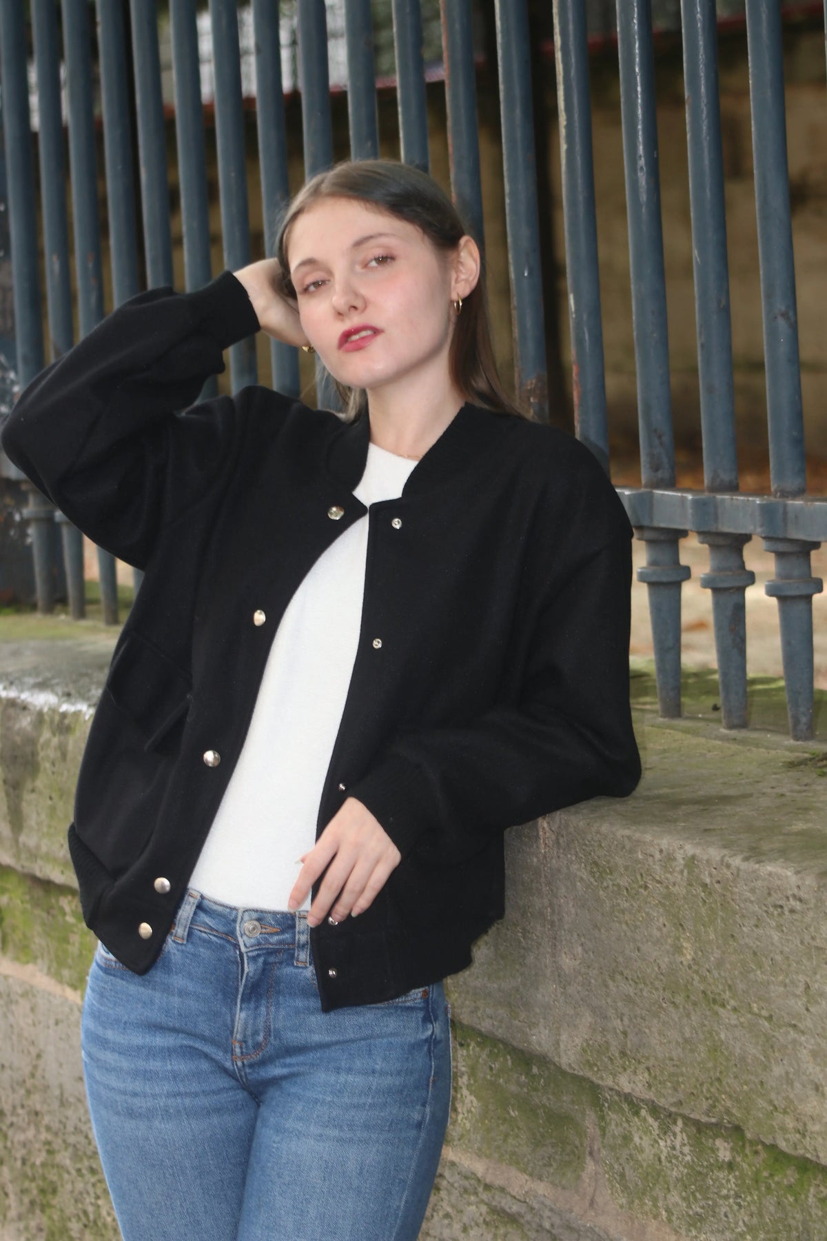 Femme portant un blouson noir style bomber, un t-shirt blanc et un jean bleu.