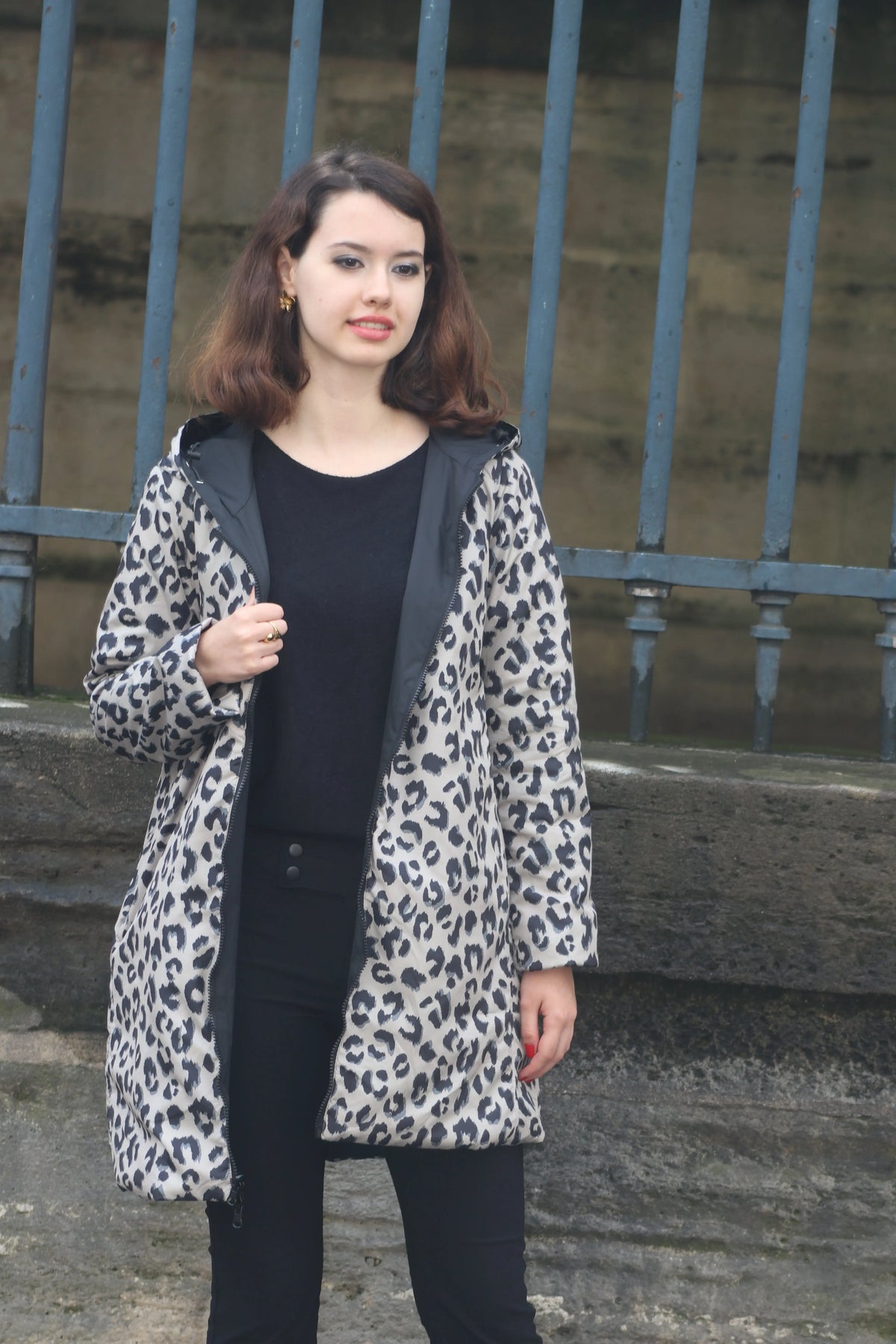 Femme portant un manteau à imprimé léopard gris et noir sur un haut et pantalon noirs.