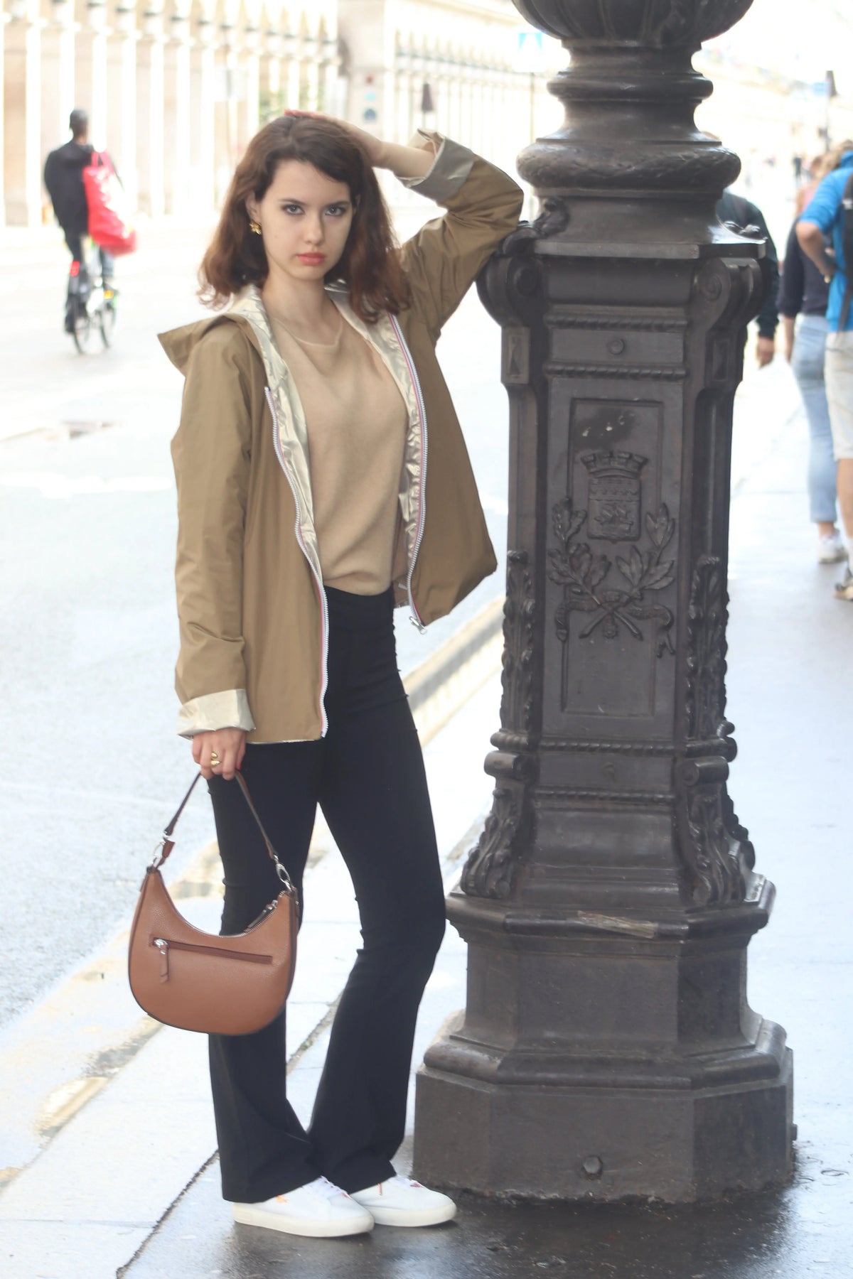 Femme portant une veste beige, pantalon noir et sac à main marron dans une rue parisienne.