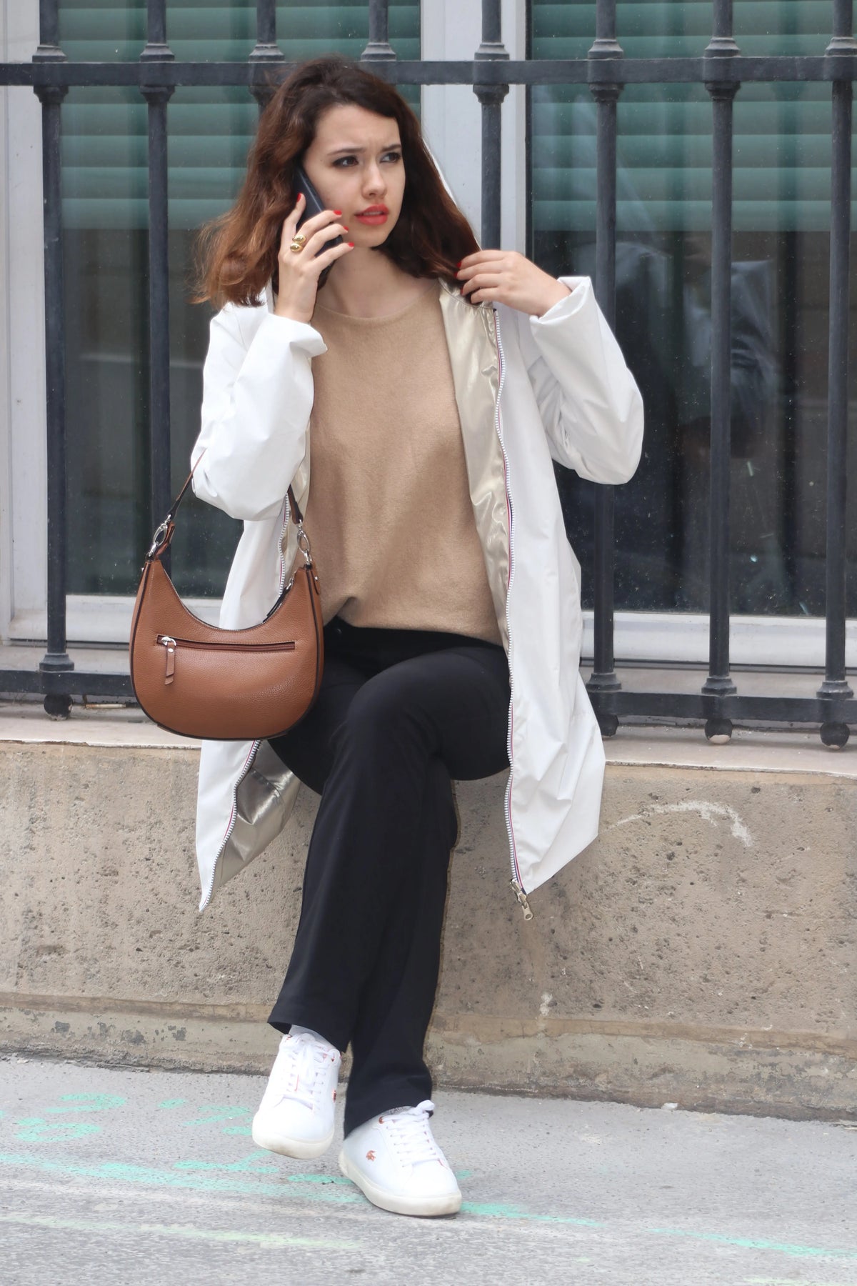 Femme avec un sac à main marron, un pull beige et un manteau blanc.