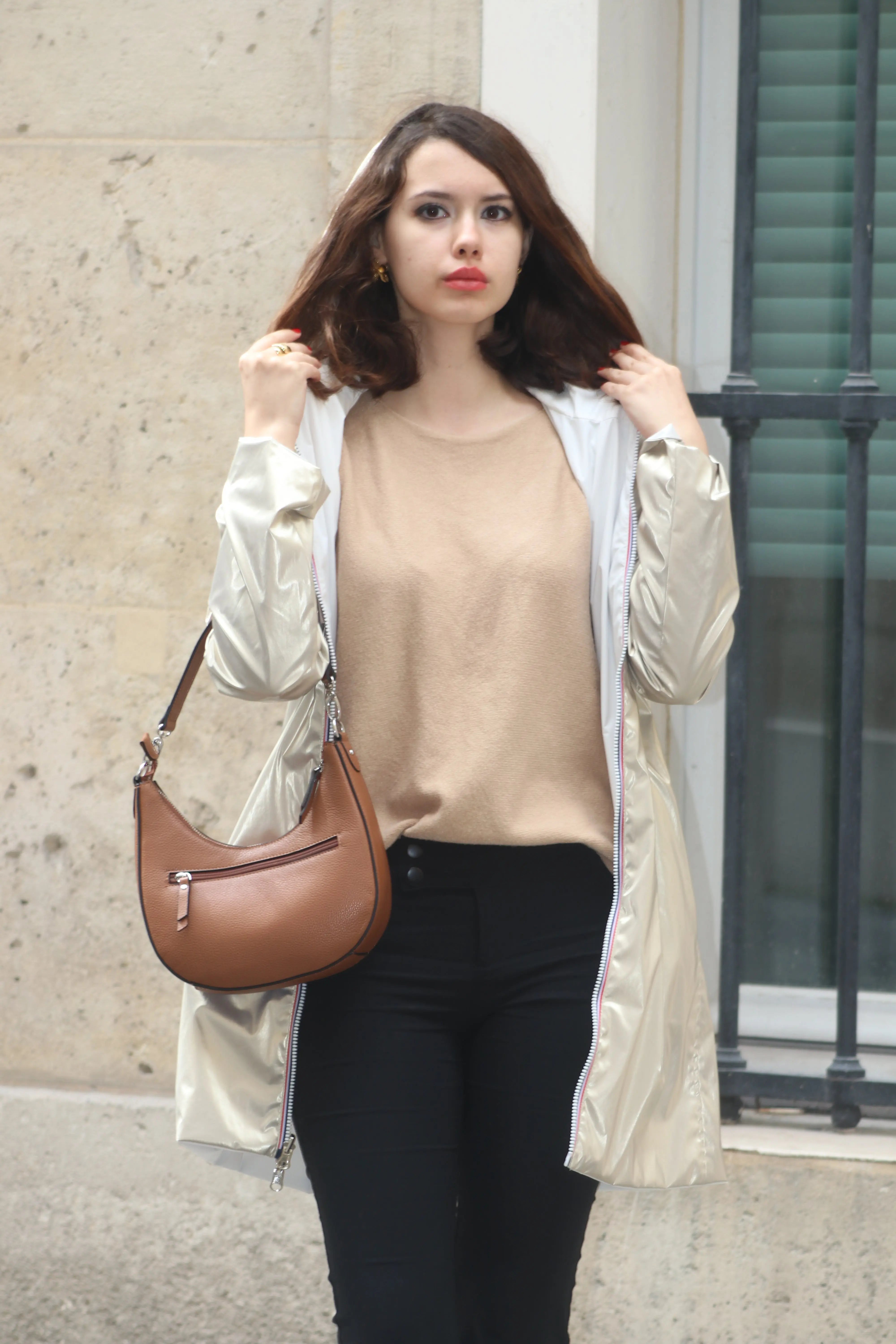 Femme portant un manteau argenté, un pull beige et un sac à main marron.