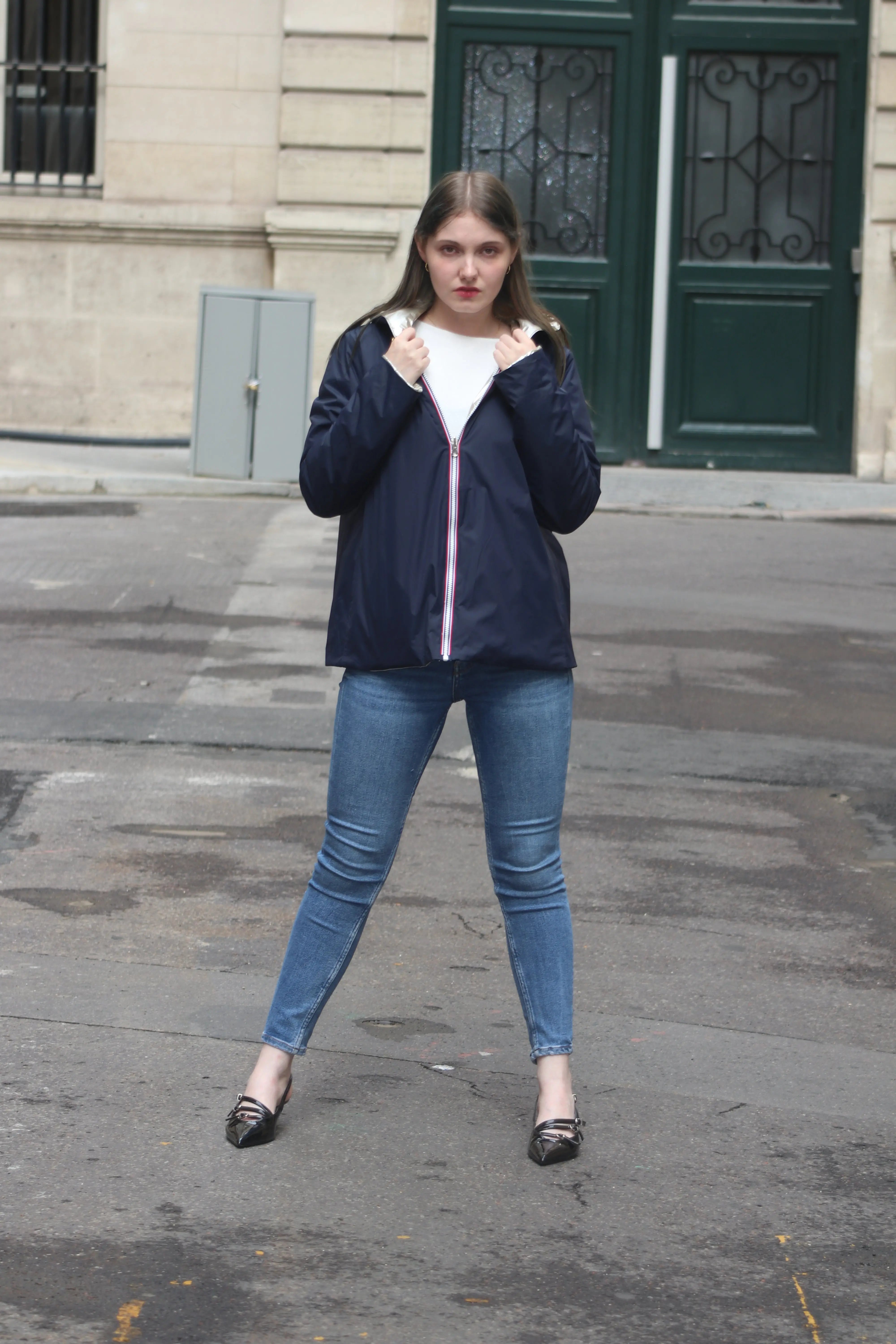 Femme portant une veste bleu marine, un t-shirt blanc et un jean bleu sur un trottoir.