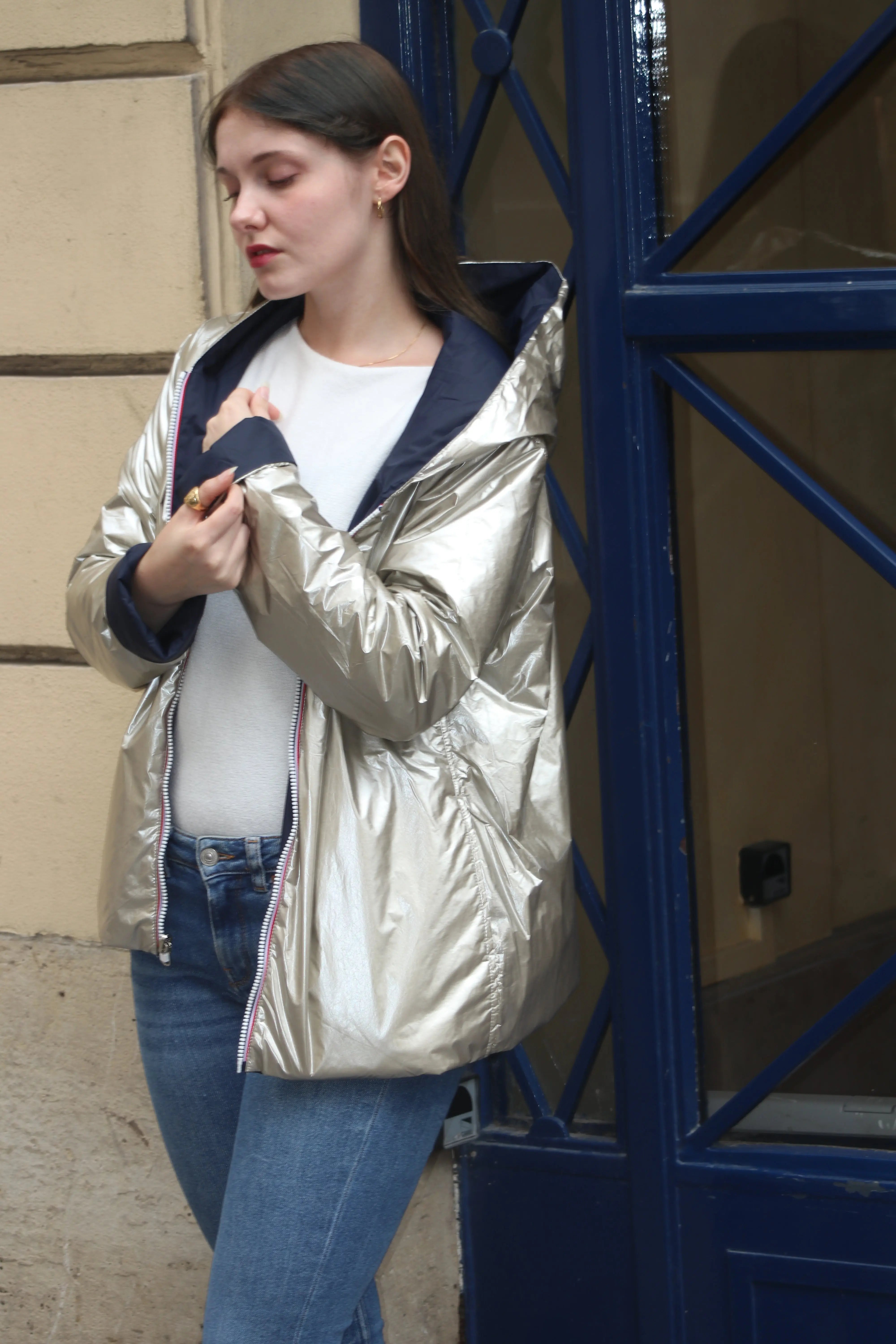 Femme portant une veste métallisée argentée avec capuche et un jean bleu.