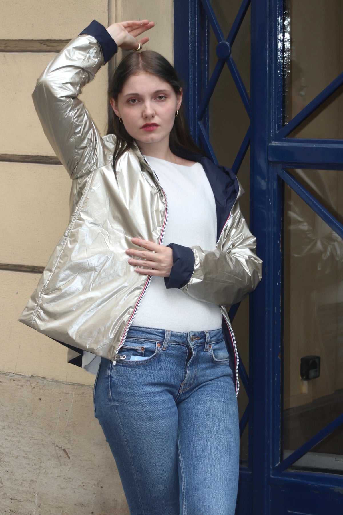 Femme portant une veste courte métallisée argentée, un t-shirt blanc et un jean bleu.