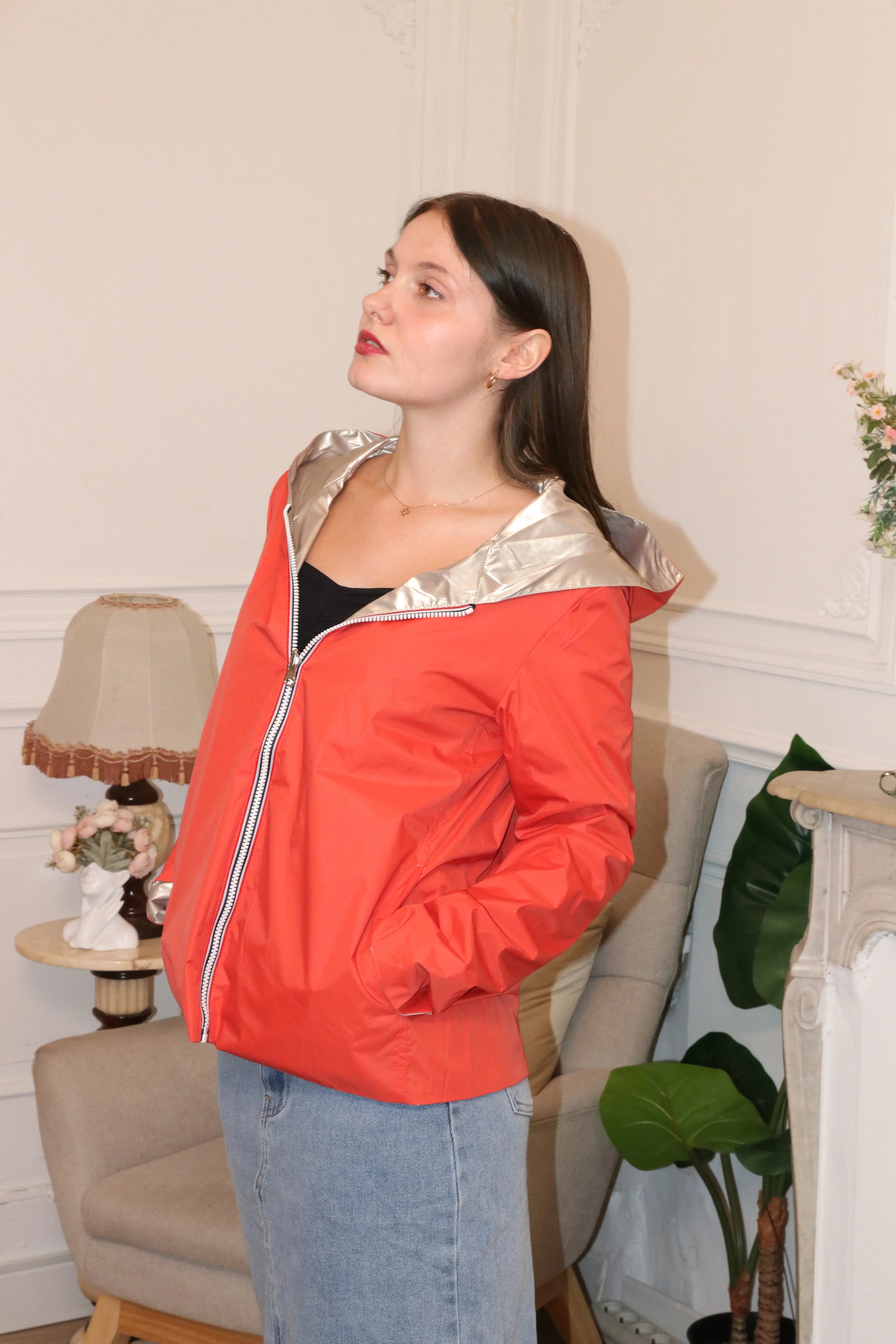 Femme portant une veste de pluie rouge corail avec capuche argentée et jupe en jean