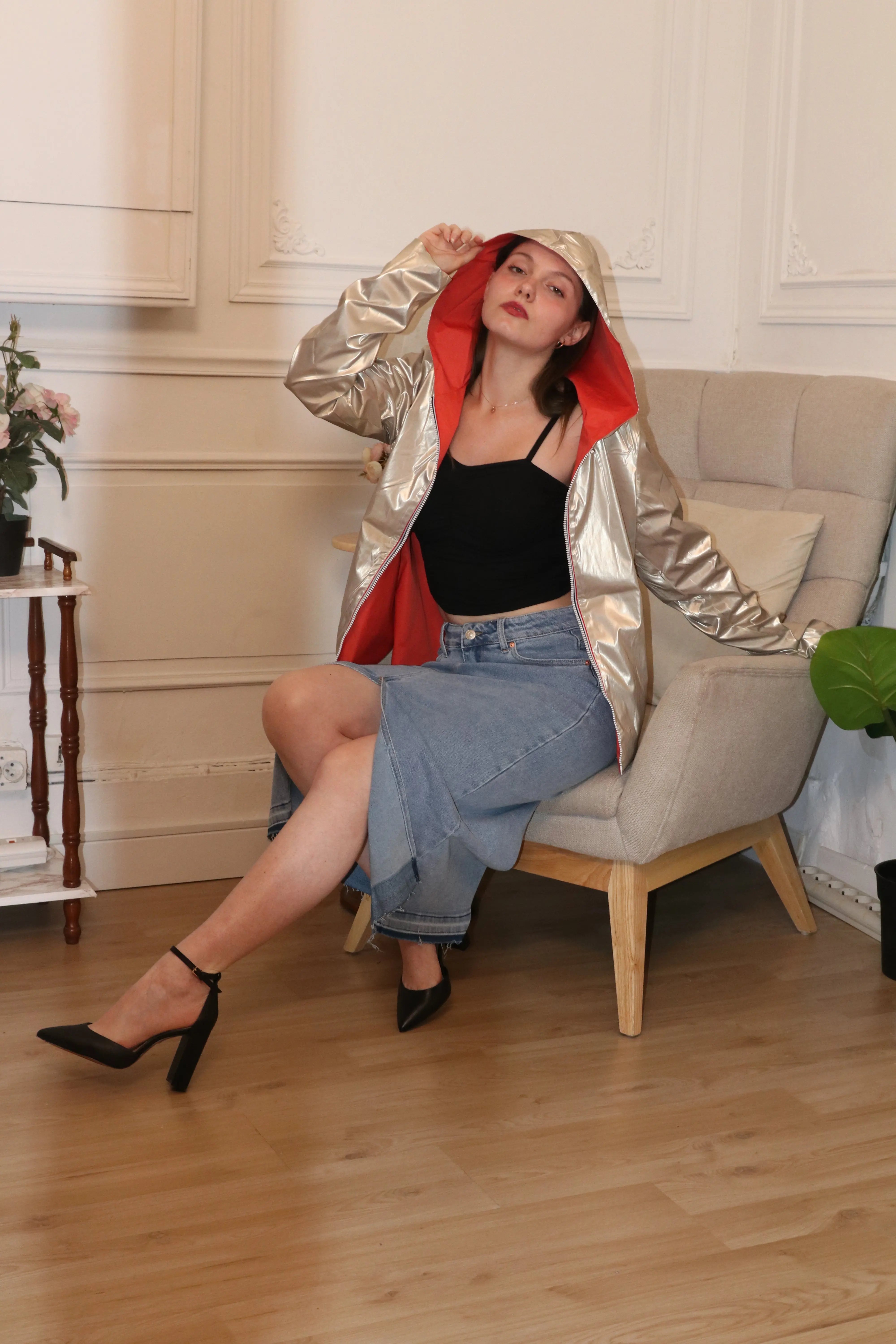 Femme portant un coupe-vent argenté avec doublure rouge, débardeur noir et jupe en jean.