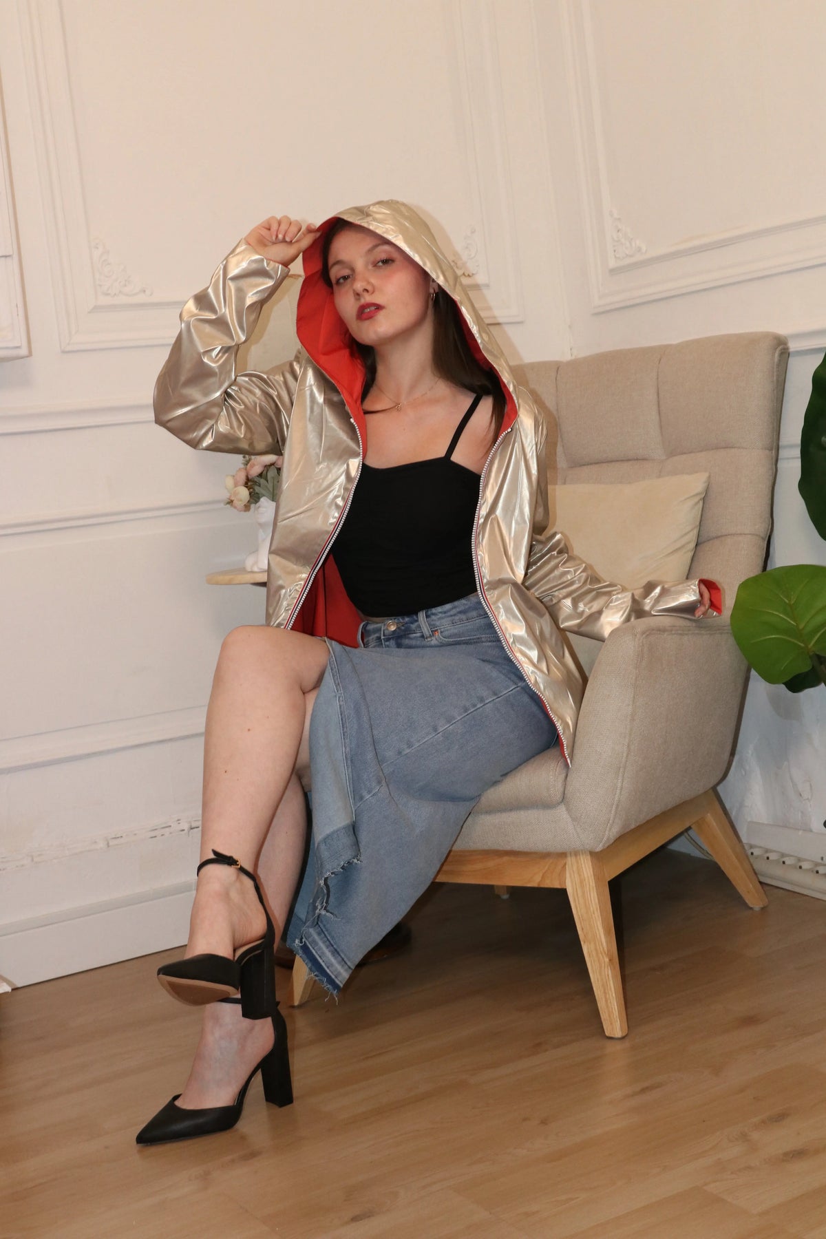 Femme portant une veste à capuche dorée métallisée, un débardeur noir et une jupe en jean.