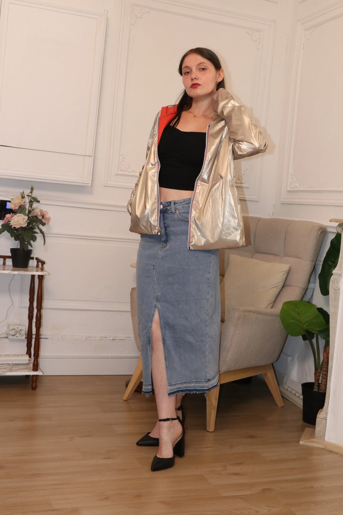 Femme portant une veste argentée métallisée, un top noir et une jupe en jean longue fendue.