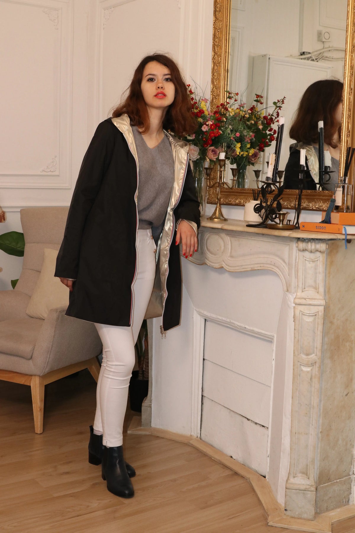 Femme portant un manteau noir avec doublure dorée, pantalon blanc et bottines noires.