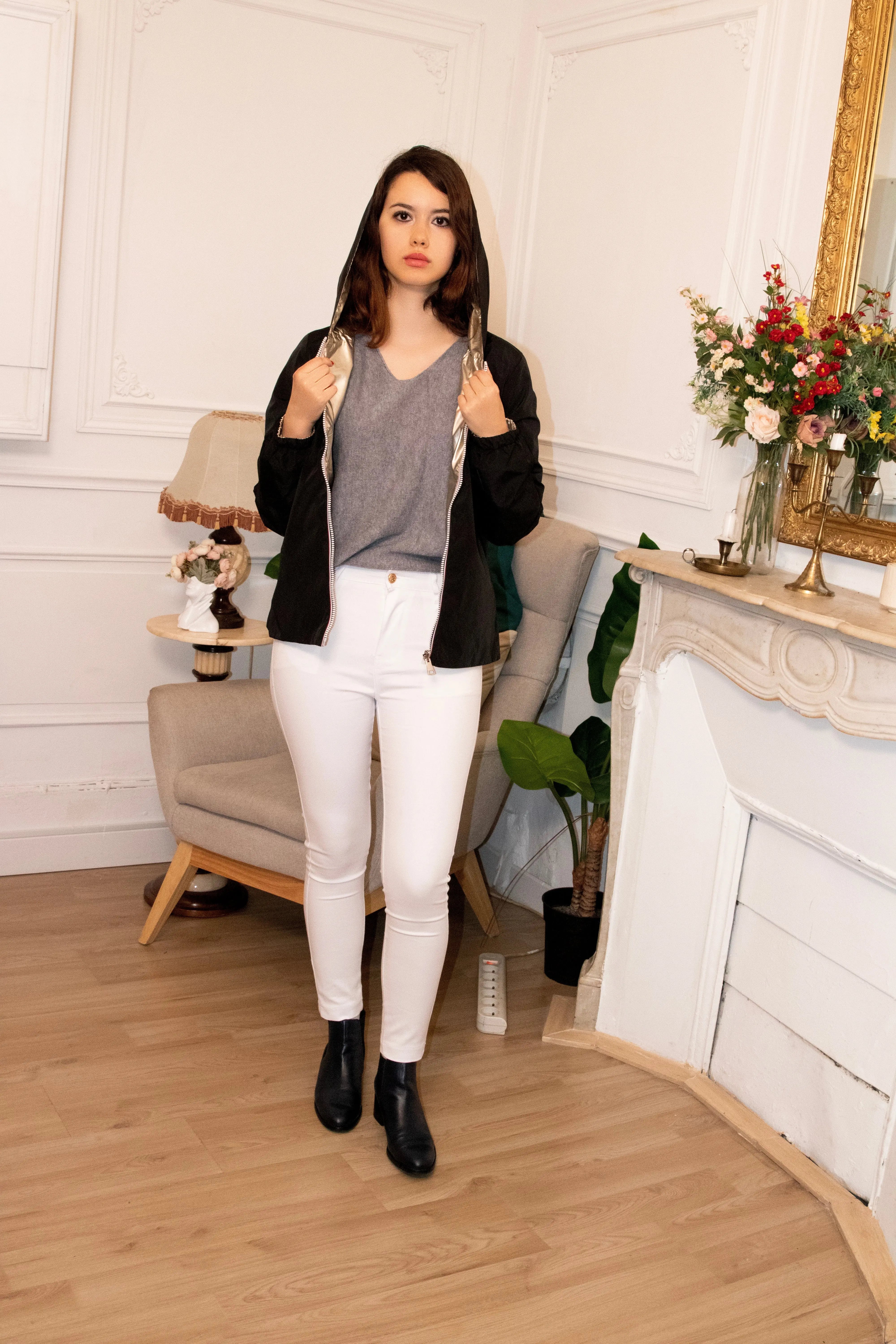 Femme portant un pantalon blanc ajusté, un haut gris et une veste noire avec capuche.